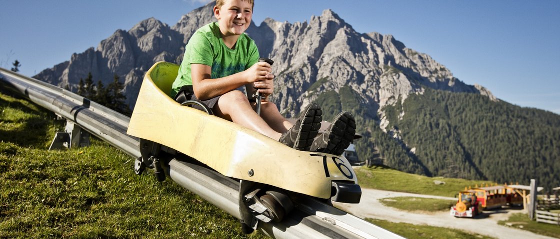 Your family hotel in Neustift im Stubaital Boy riding summer toboggan on a track with mountains in the background on a sunny day