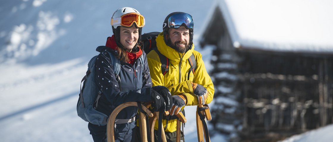 Gaudi im Winterurlaub im Stubaital Paar in Winterkleidung mit Schlitten vor verschneitem Haus