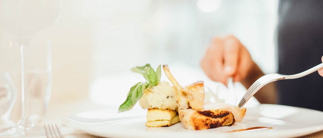 The secret to an indulgent holiday Person cutting gourmet dish with mashed potatoes and basil on white plate