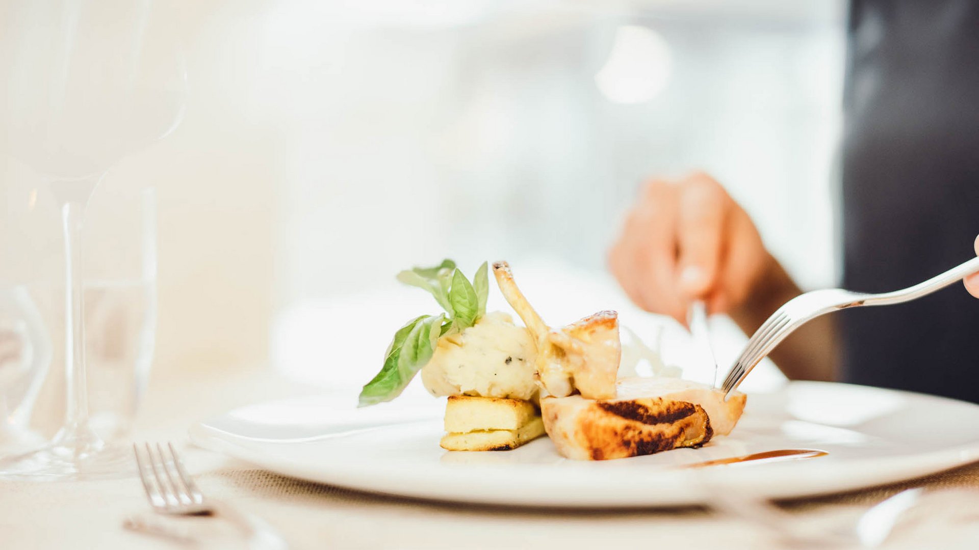 The secret to an indulgent holiday Person cutting gourmet dish with mashed potatoes and basil on white plate