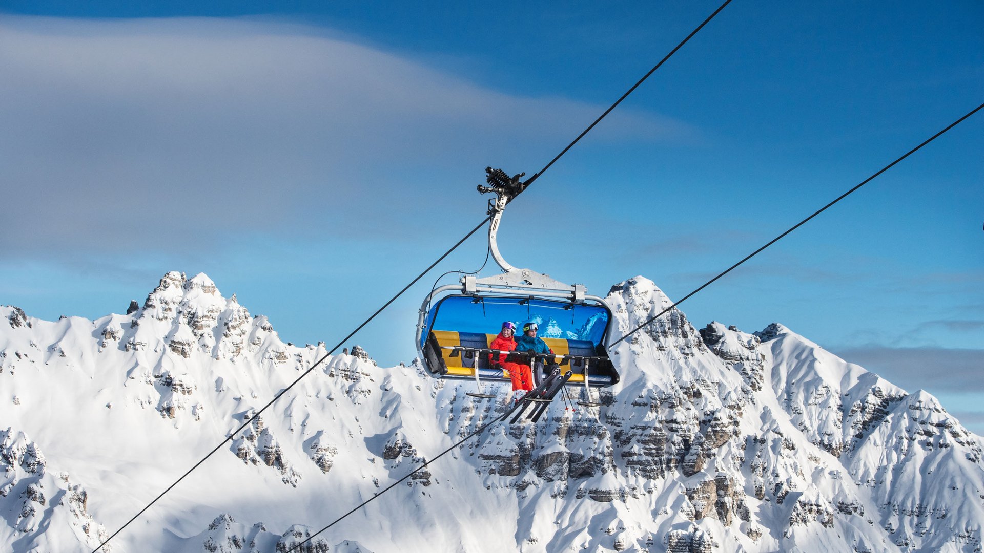 Spannendes rund ums Aktivhotel im Stubaital Skilift mit zwei Skifahrern vor schneebedeckten Bergen und blauem Himmel
