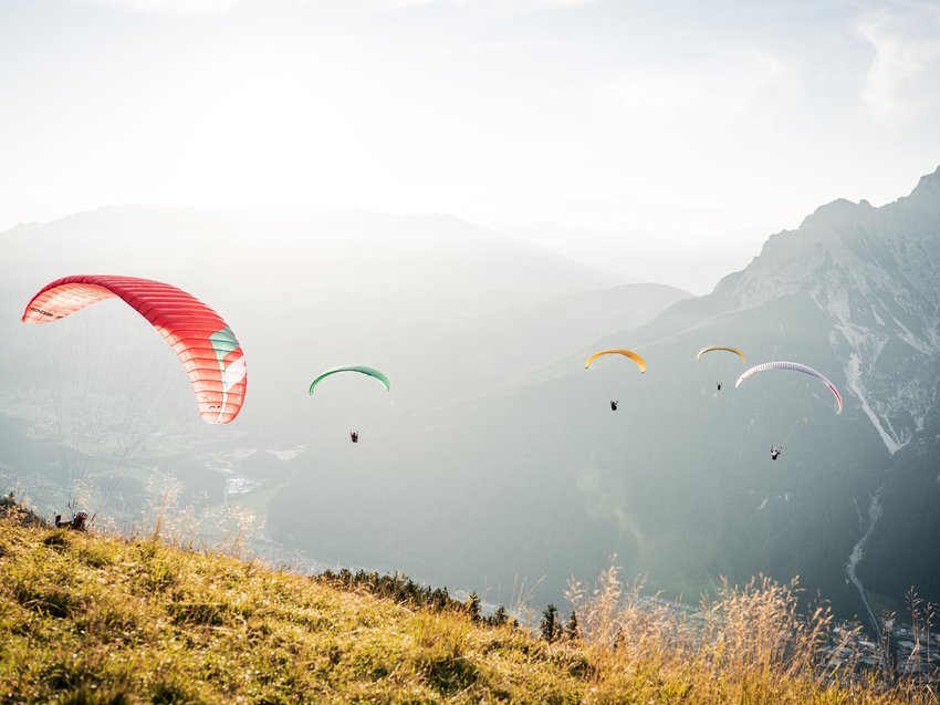 Radelspaß im Bike-Hotel in Tirol Fünf Gleitschirmflieger über sonnigem Bergwiesenhang mit Bergpanorama im Hintergrund