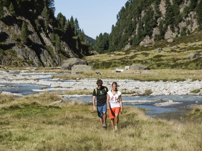 Mountain love at our hiking hotel in Stubaital Couple hiking on grassy path beside mountain stream in landscape with trees and hills