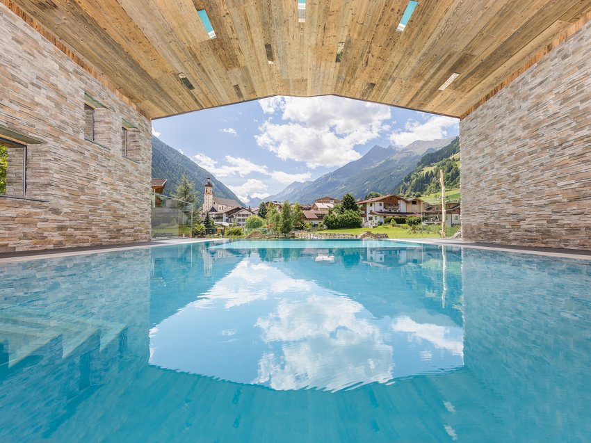 Ein B&B Hotel im Stubaital mit Halbpension-Möglichkeit Überdachter Pool mit Blick auf ein malerisches Dorf und Berge unter blauem Himmel