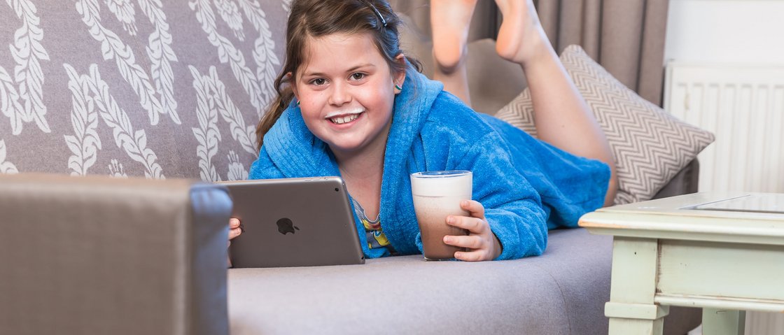 Your family hotel in Neustift im Stubaital Girl in blue bathrobe with milk mustache drinking milk and holding tablet on sofa