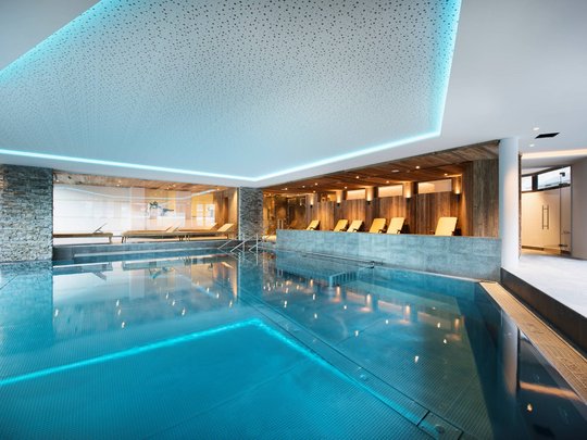 Your wellness hotel in Neustift im Stubaital awaits Modern indoor pool with turquoise water, loungers and wood paneling