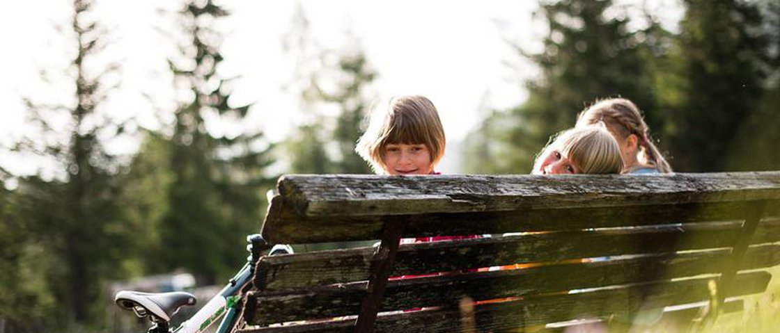 Willkommen im Hotel in Neustift im Stubaital! Drei Kinder sitzen auf einer Bank im Freien mit einem Fahrrad daneben