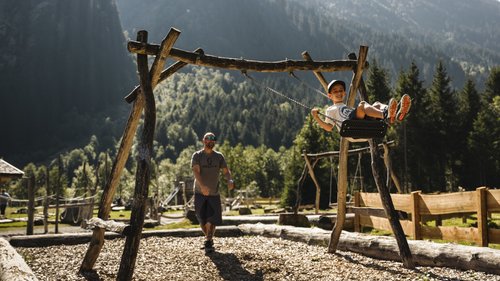 Enquire about your B&B mountain holiday here Boy swinging pushed by adult on a playground surrounded by mountains and trees