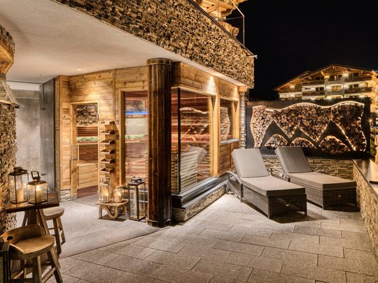 Your wellness hotel in Neustift im Stubaital awaits Illuminated outdoor area with sauna, loungers and stacked firewood at night