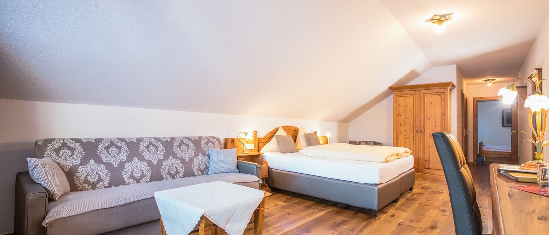 Your family hotel in Neustift im Stubaital Cozy hotel room with sofa, double bed, and wooden furniture under slanted ceiling