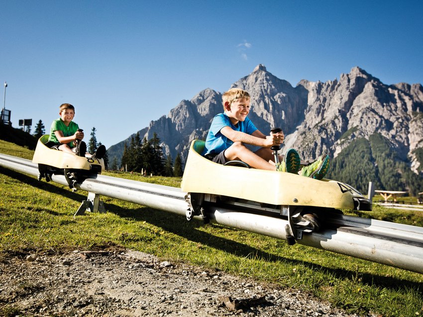B&B Hotel mit Stubai Super Card Zwei Jungen fahren auf Alpenrodelbahn vor Bergkulisse bei Sonnenschein