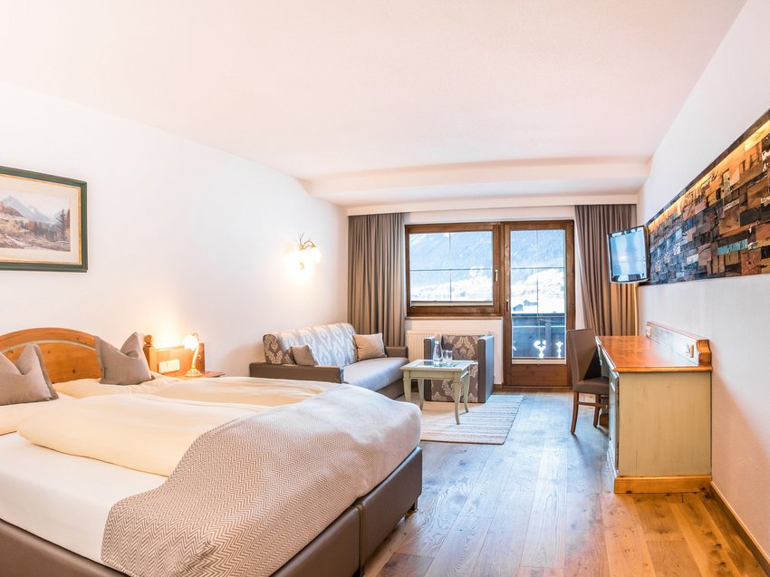 Welcome to our hotel in Neustift im Stubaital! Bright hotel room with double bed, sofa, desk and mountain view through window
