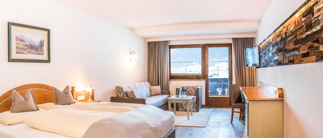 Welcome to our hotel in Neustift im Stubaital! Bright hotel room with double bed, sofa, desk and mountain view through window