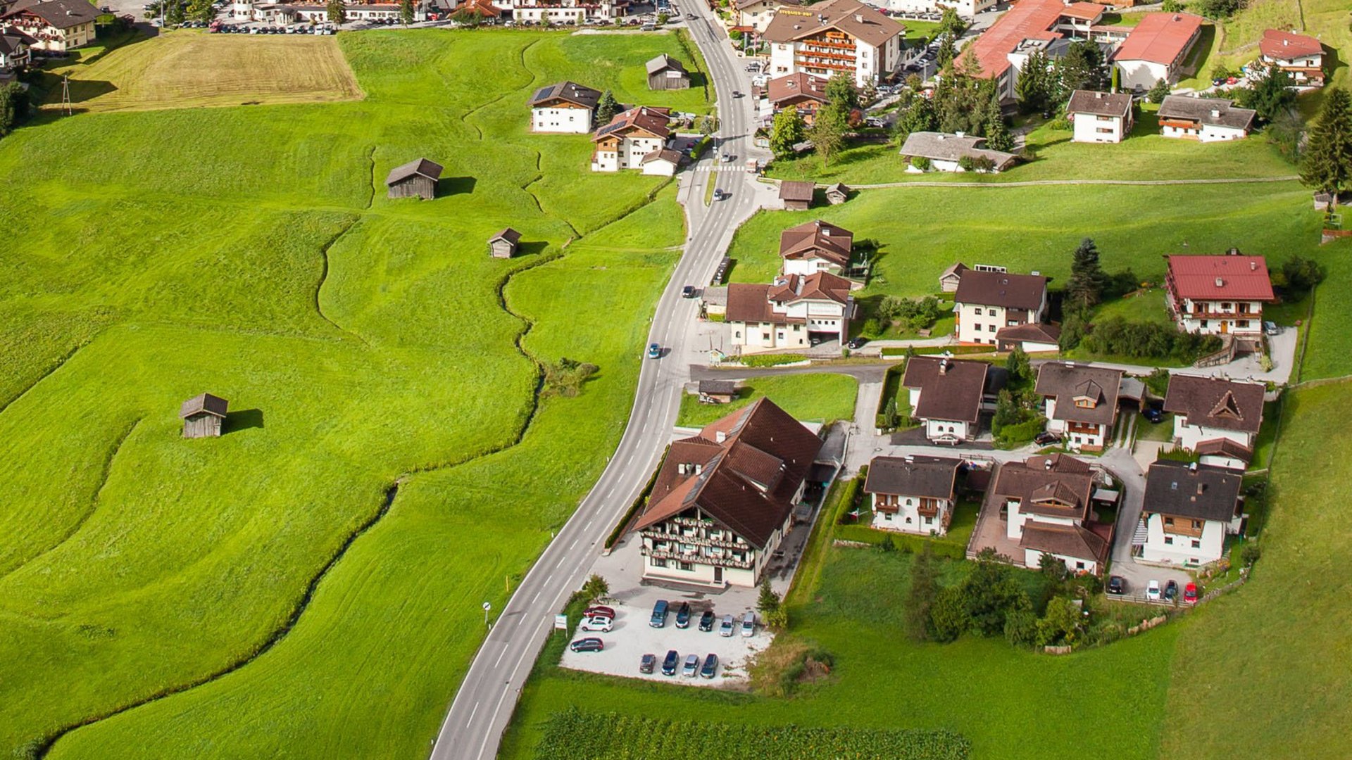 Luftaufnahme eines Dorfes im Tal mit grünen Wiesen und umgebenden Bergen