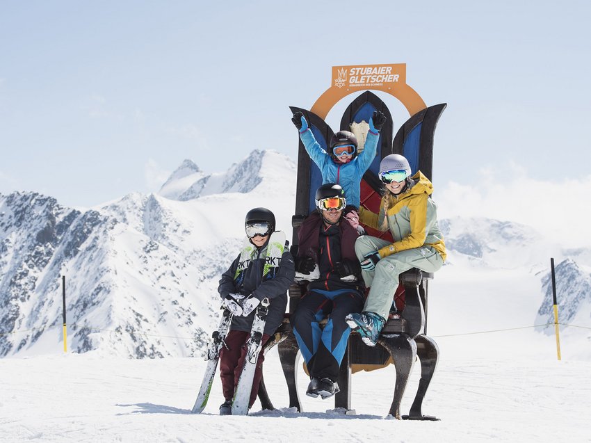 Ein B&B Hotel im Stubaital mit Halbpension-Möglichkeit Familie mit Skihelmen sitzt auf einem großen Stuhl vor verschneiten Bergen in Stubai