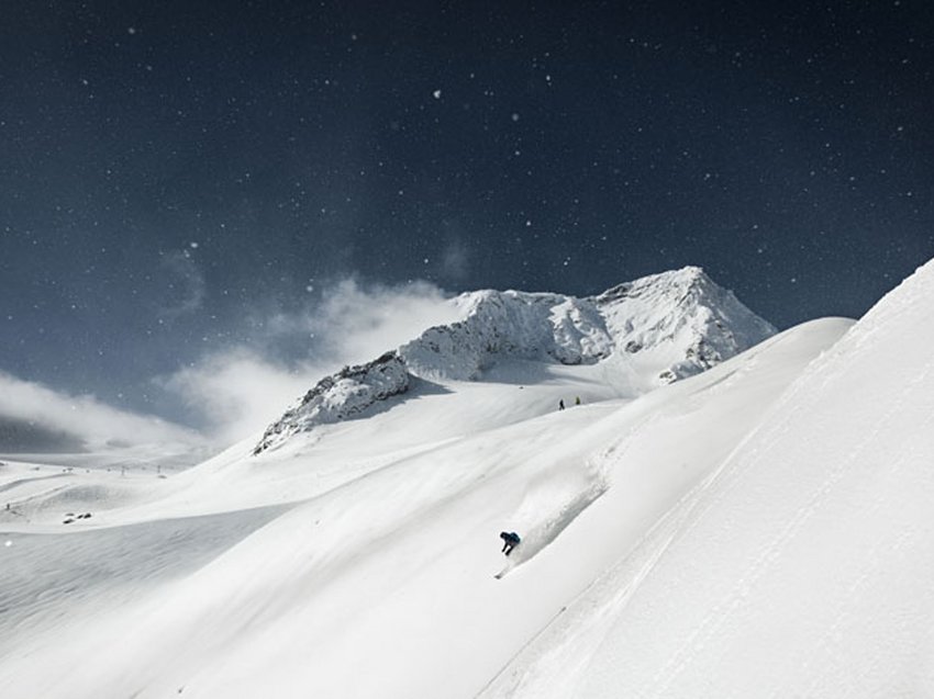 A B&B hotel at the Stubai Glacier Skier descending steep snow-covered mountain slope under cloudy sky