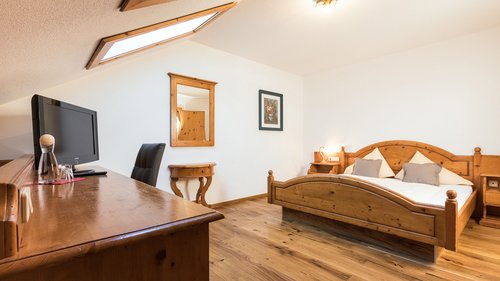 Enquire about your B&B mountain holiday here Cozy hotel room with wooden furniture, double bed, and desk under slanted ceiling