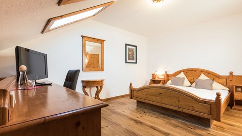 Enquire about your B&B mountain holiday here Cozy hotel room with wooden furniture, double bed, and desk under slanted ceiling