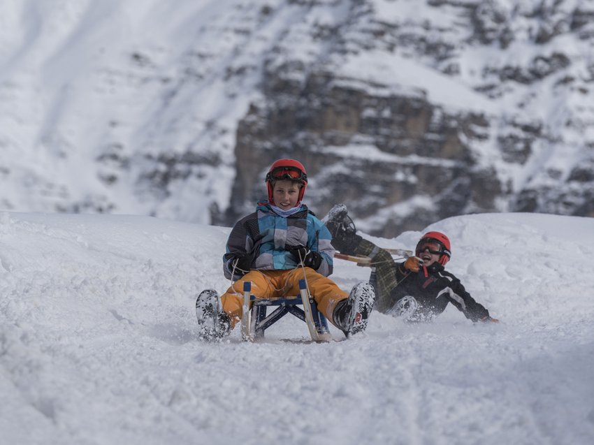 Gaudi im Winterurlaub im Stubaital Zwei Kinder rodeln im Schnee mit Bergen im Hintergrund