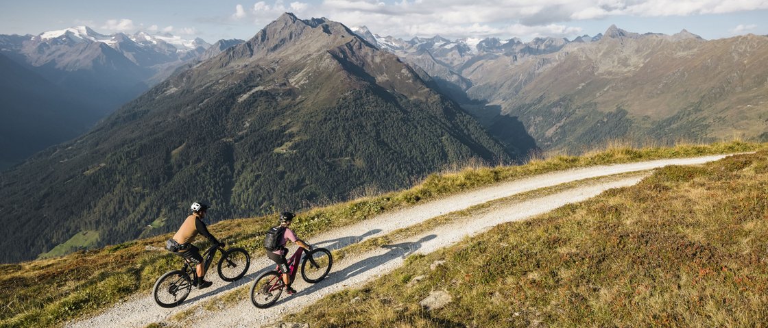Radelspaß im Bike-Hotel in Tirol Zwei Mountainbiker fahren auf einem Bergweg mit Alpenpanorama im Hintergrund