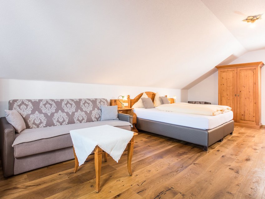 How to make your holiday in Stubaital unforgettably amazing Cozy guest room with bed, sofa, and wooden wardrobe under a slanted ceiling