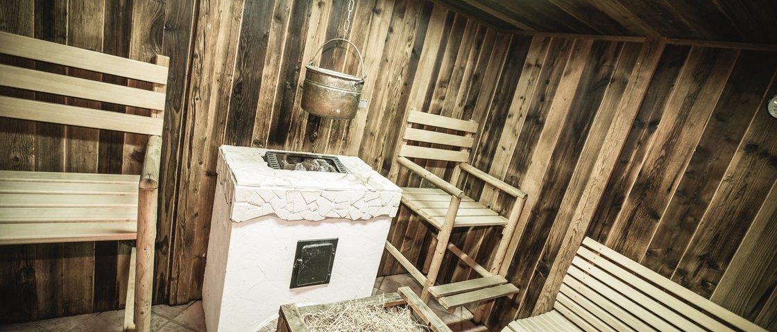 Your wellness hotel in Neustift im Stubaital awaits Sauna room with wooden benches, wood stove, and a hanging metal pot