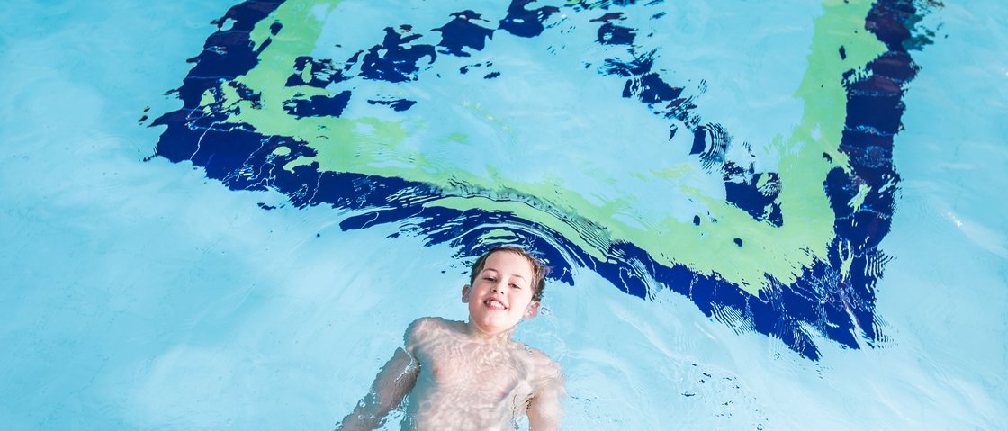 Ab ins Wellnesshotel in Neustift im Stubaital Junge schwimmt entspannt auf dem Rücken im Schwimmbadwasser