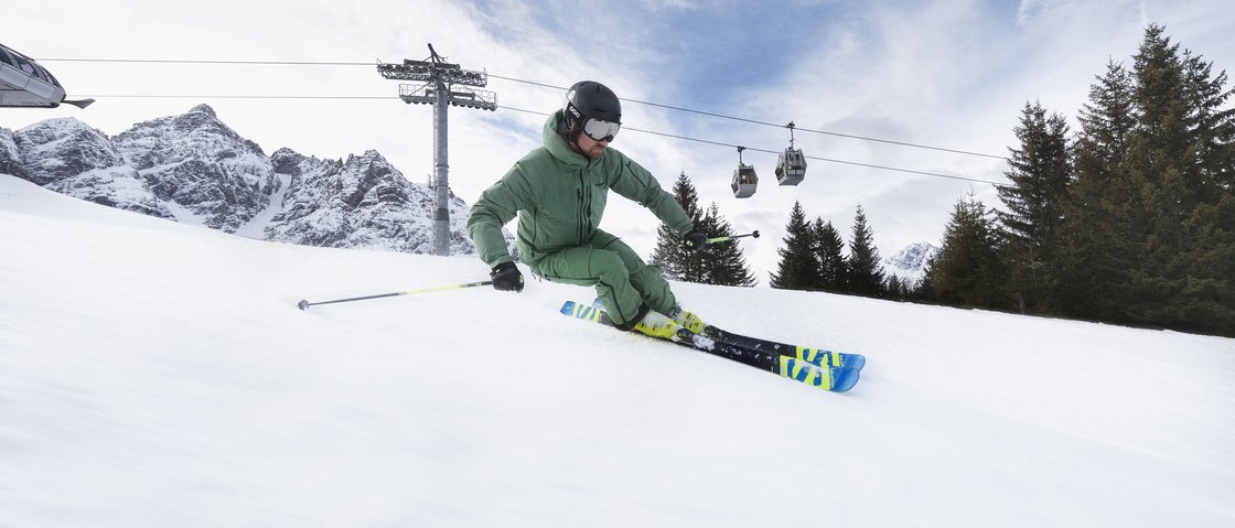 Dream days at our ski hotel in Stubaital Skier in green jacket skiing down snowy mountain with cable cars in background