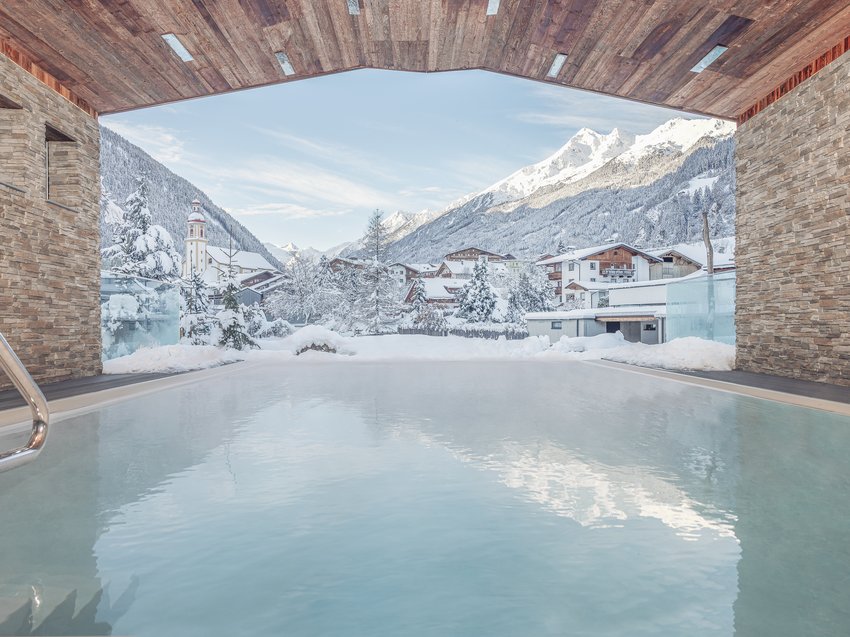 Ein B&B Hotel im Stubaital mit Halbpension-Möglichkeit Pool mit Blick auf ein verschneites Alpendorf und schneebedeckte Berge