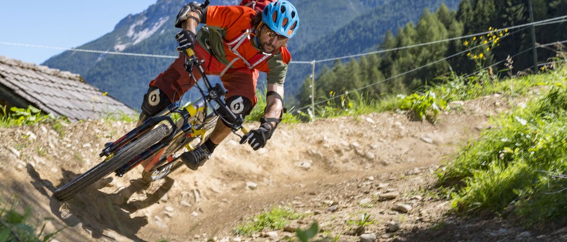 Radelspaß im Bike-Hotel in Tirol Mann fährt Mountainbike schnell auf kurvigem Gebirgspfad mit Helm und Schutzkleidung