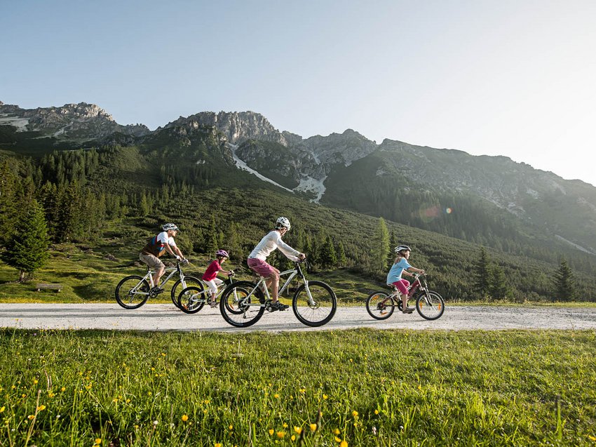 Radelspaß im Bike-Hotel in Tirol Familie fährt Fahrräder auf einem Bergweg bei sonnigem Wetter