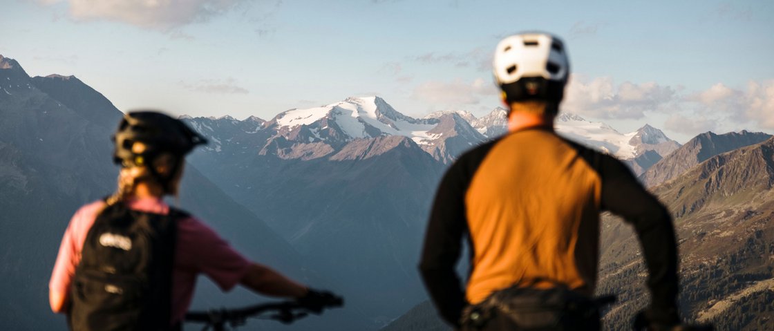 Radelspaß im Bike-Hotel in Tirol Zwei Mountainbiker mit Helmen schauen auf verschneite Berge und Tal